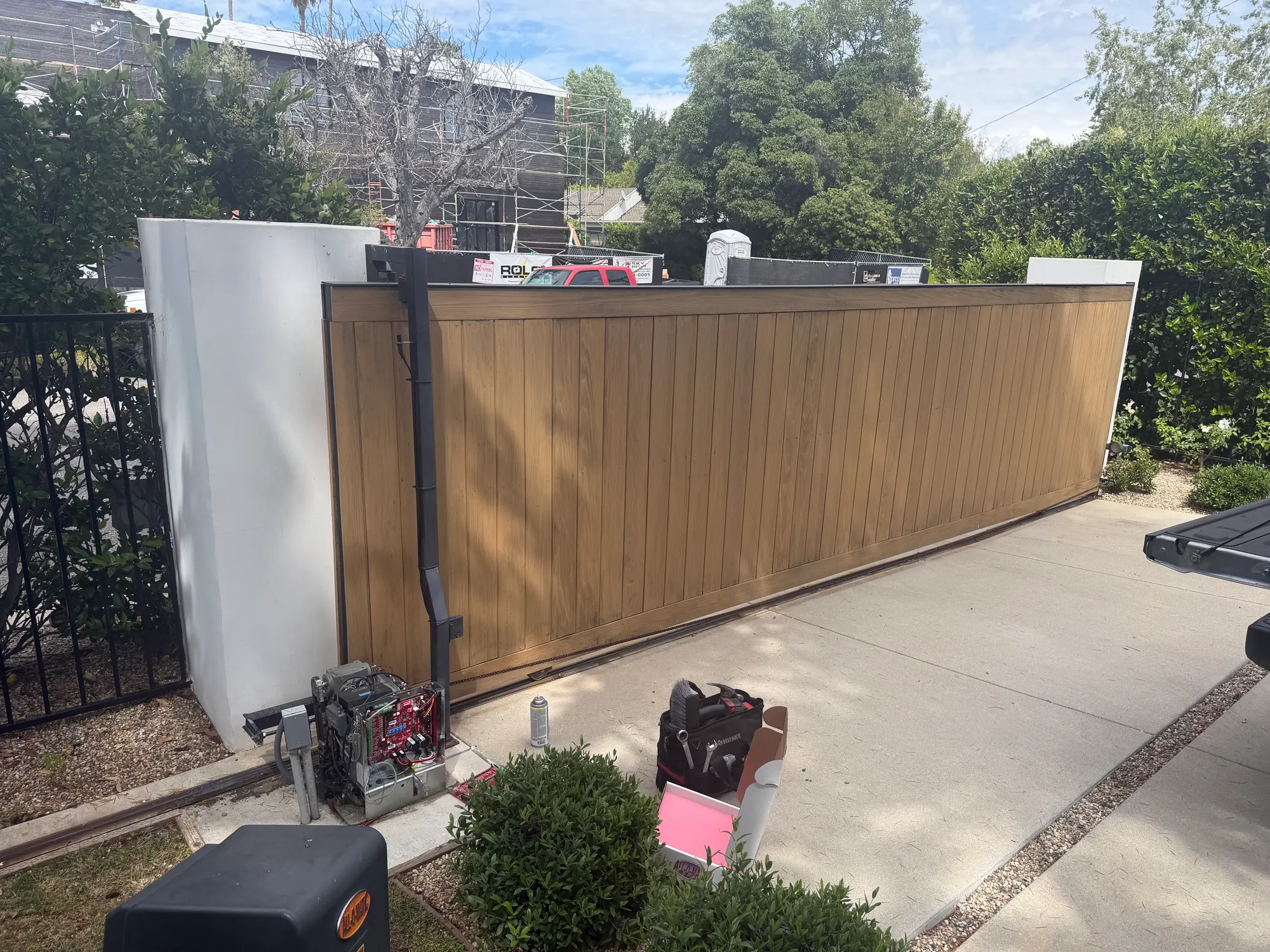 A wide timber-clad sliding gate closed across a driveway, with the slide operator mounted on the pad to the right