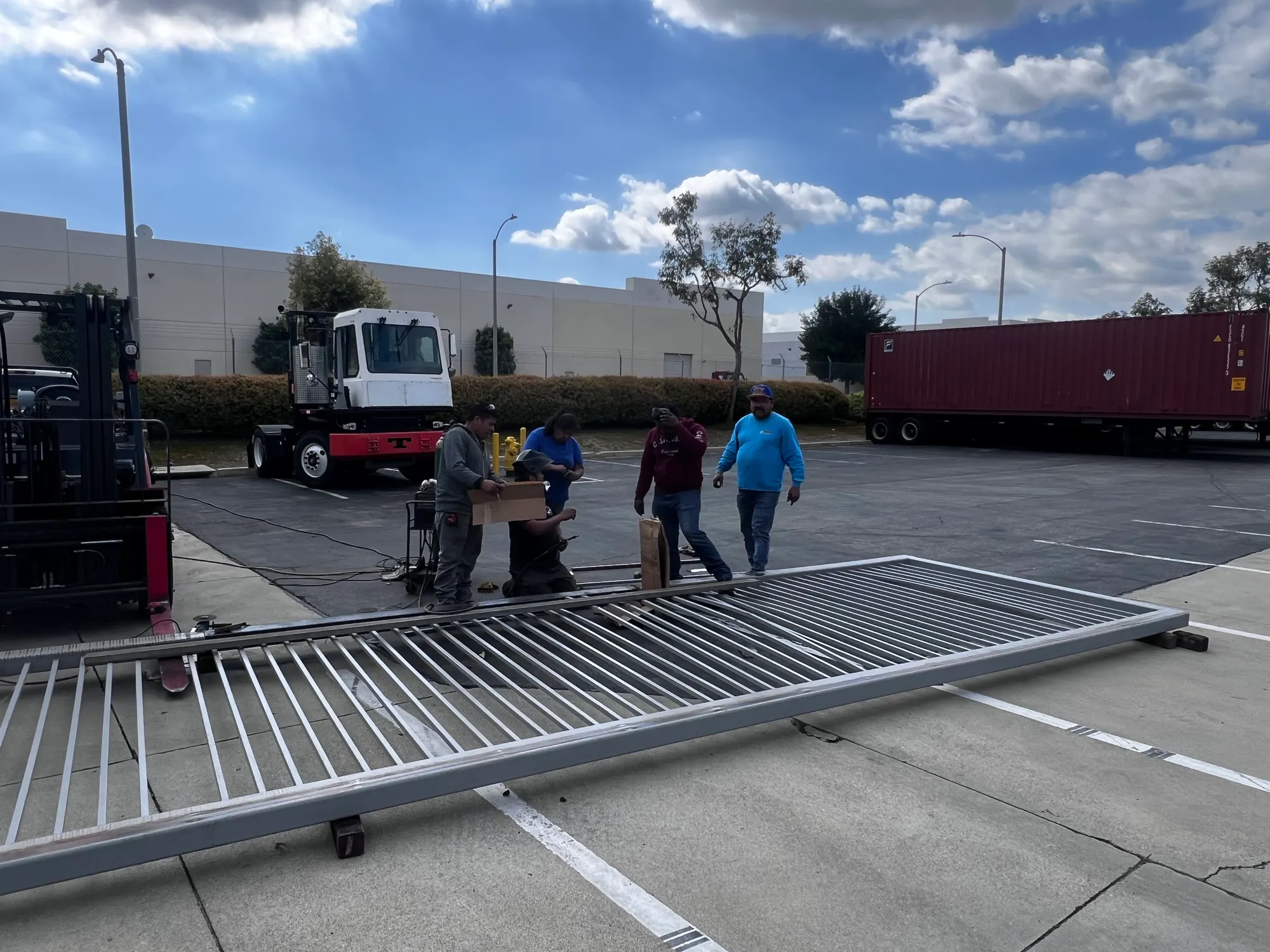 A crew lifting the long steel gate with a telehandler in the yard of a distribution facility
