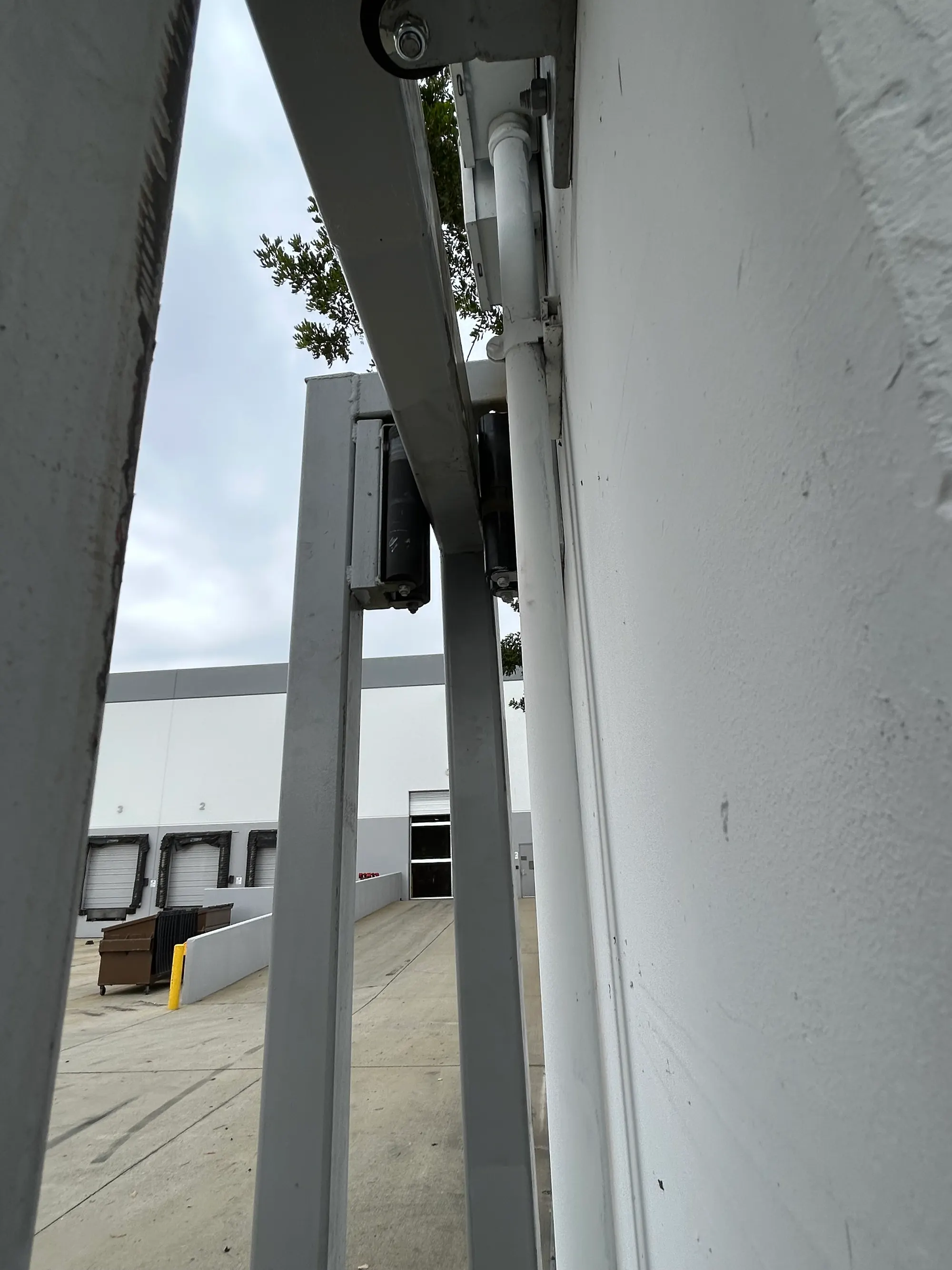 A heavy steel gate post with its mounting bracket, viewed from below against the sky