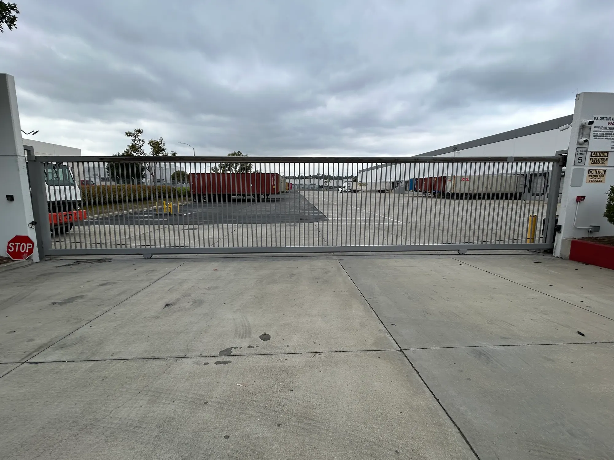 The completed slide gate open across the warehouse entrance, with the yard and shipping containers beyond