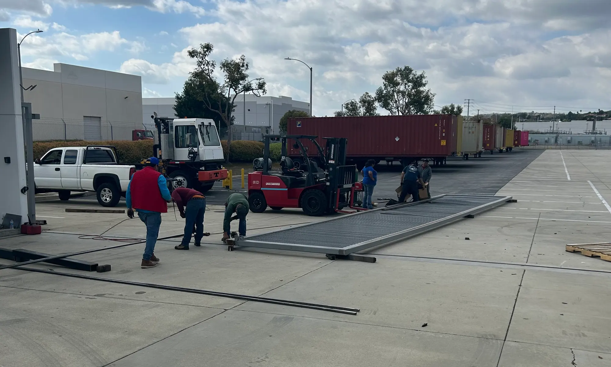 Technicians working on the gate on the ground beside a telehandler and forklift at the loading yard