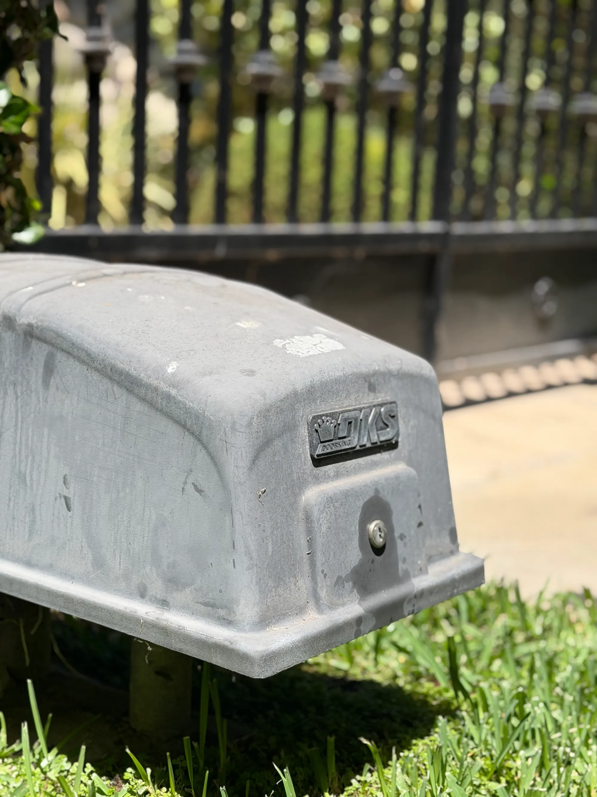 Close view of a DKS DoorKing gate operator in its cast grey housing, mounted at ground level beside a driveway gate