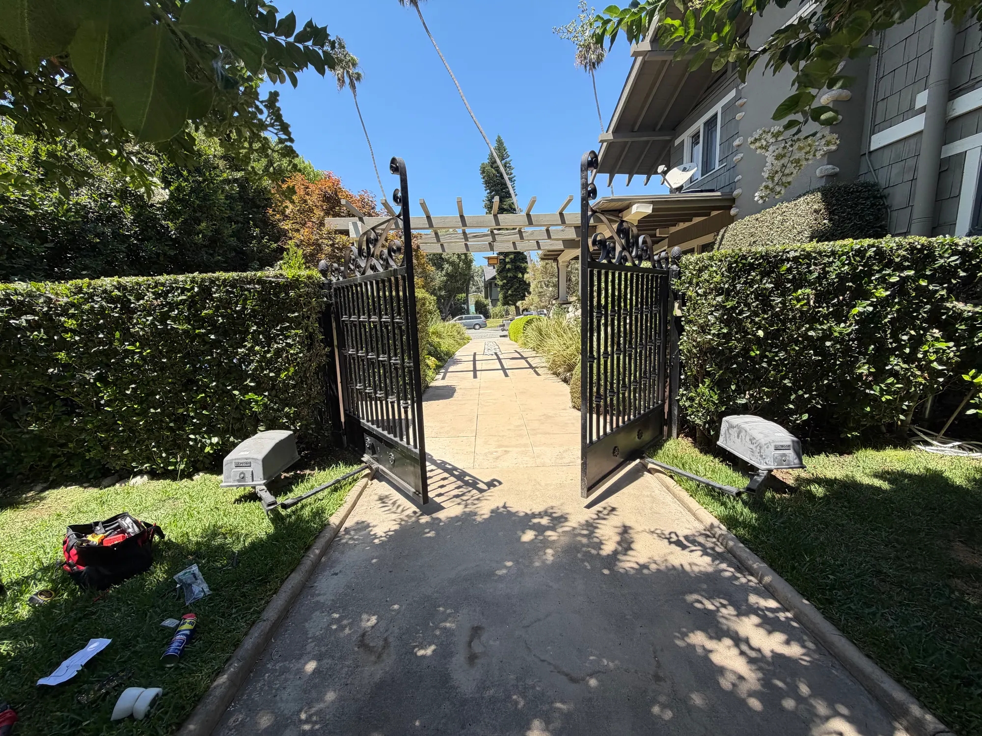 The same iron swing gates standing open, showing the driveway running between hedges toward the house