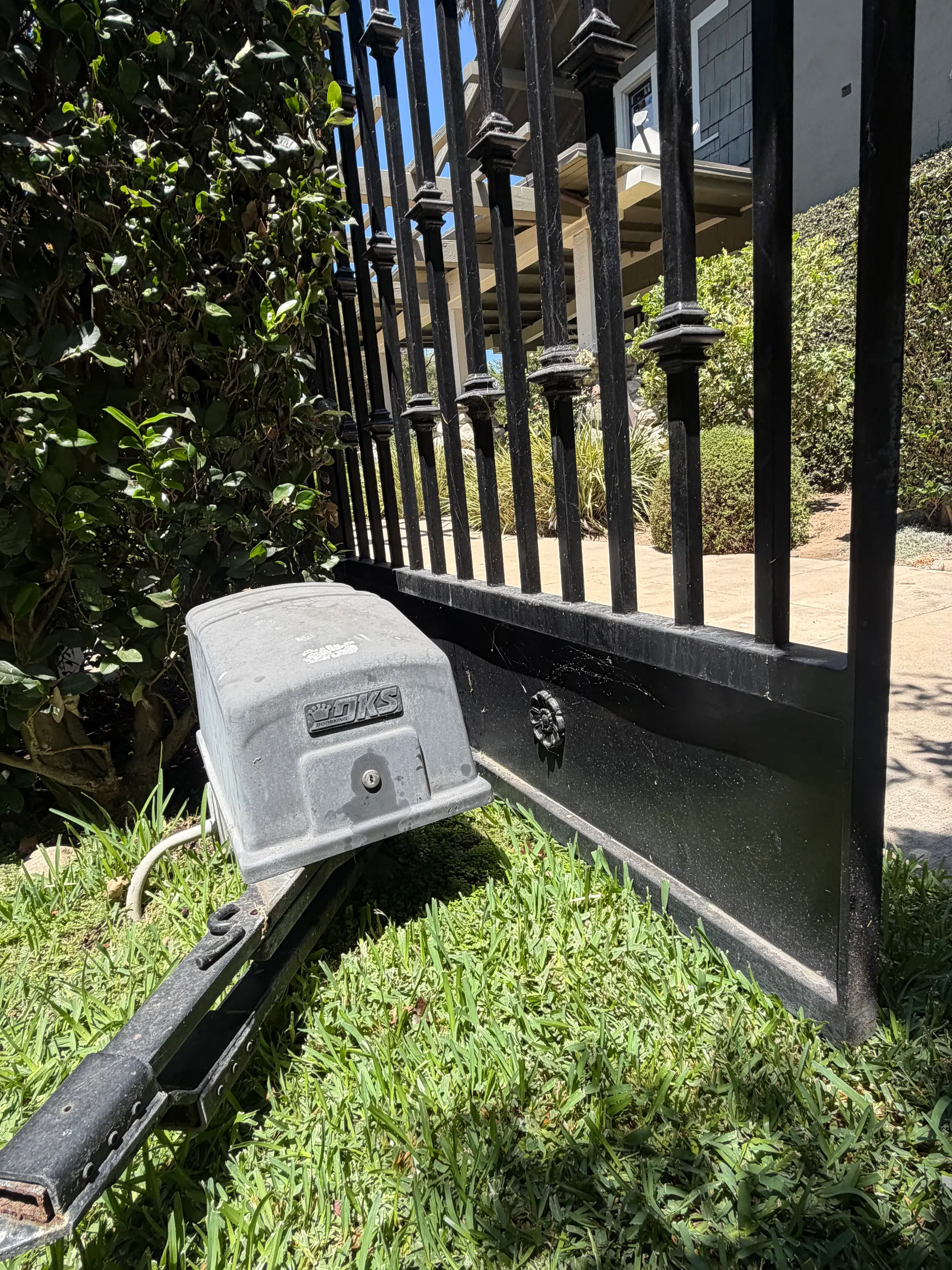 A DoorKing operator and its drive linkage connected to the lower rail of an iron swing gate leaf