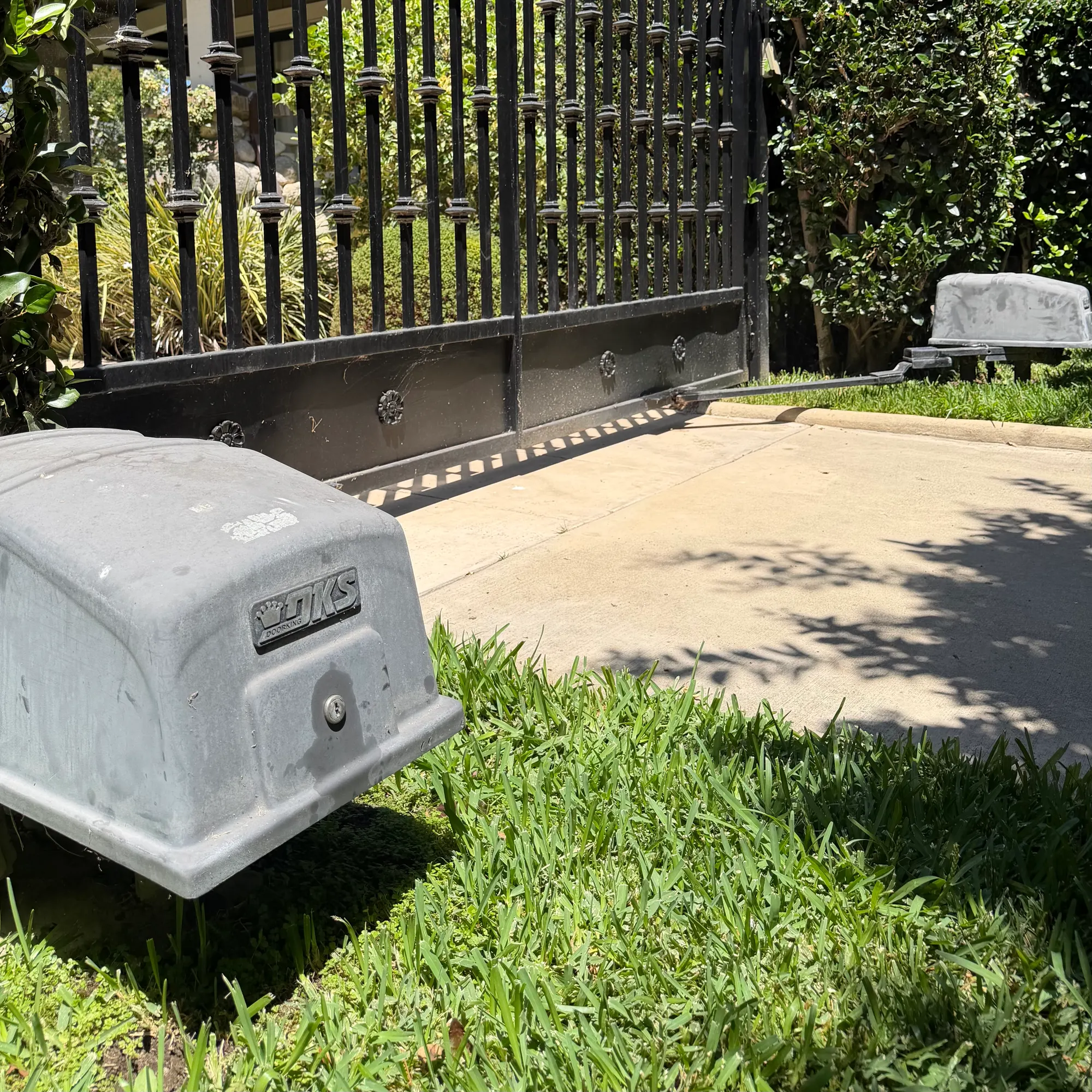 A DoorKing operator housing set on the grass beside an open swing gate, with the drive arm extended
