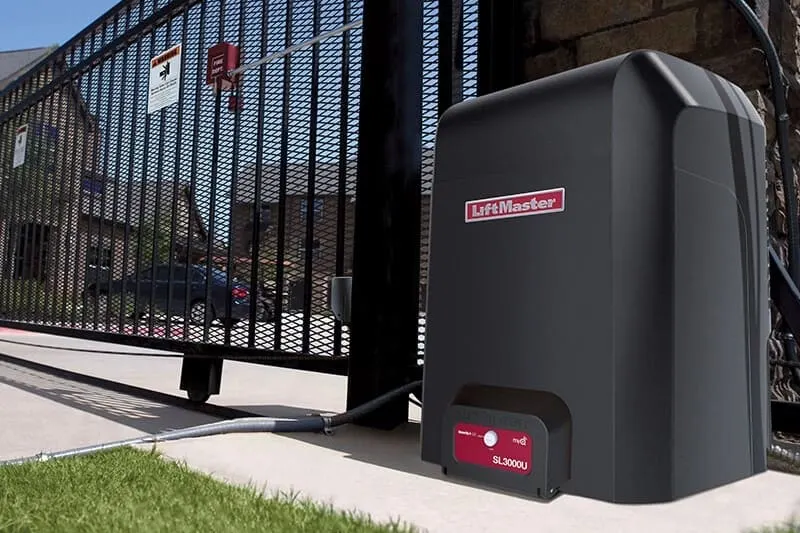 A LiftMaster slide gate operator in a black weatherproof housing beside an ornamental iron driveway gate