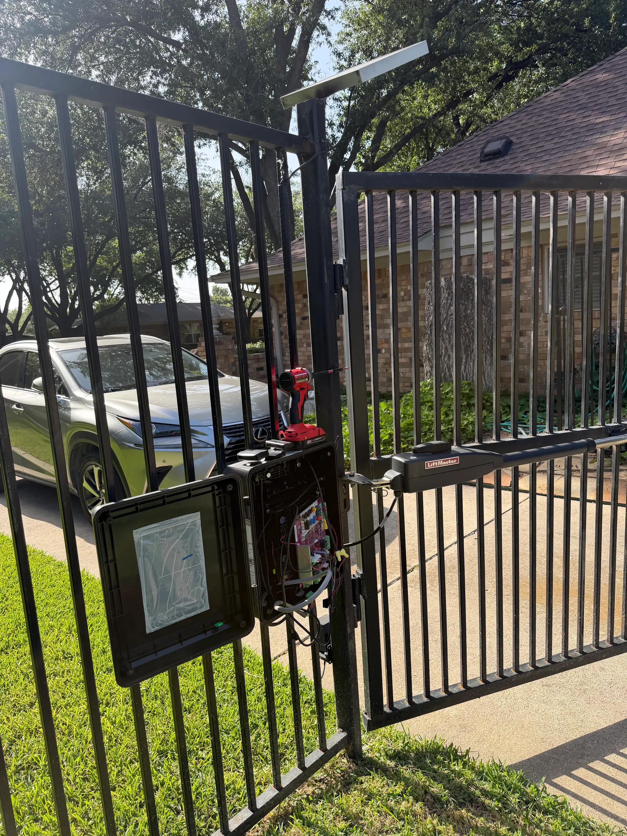 Close view of the opened LiftMaster control enclosure showing the circuit board, wiring loom and battery compartment, with the operator arm attached to the gate frame behind it