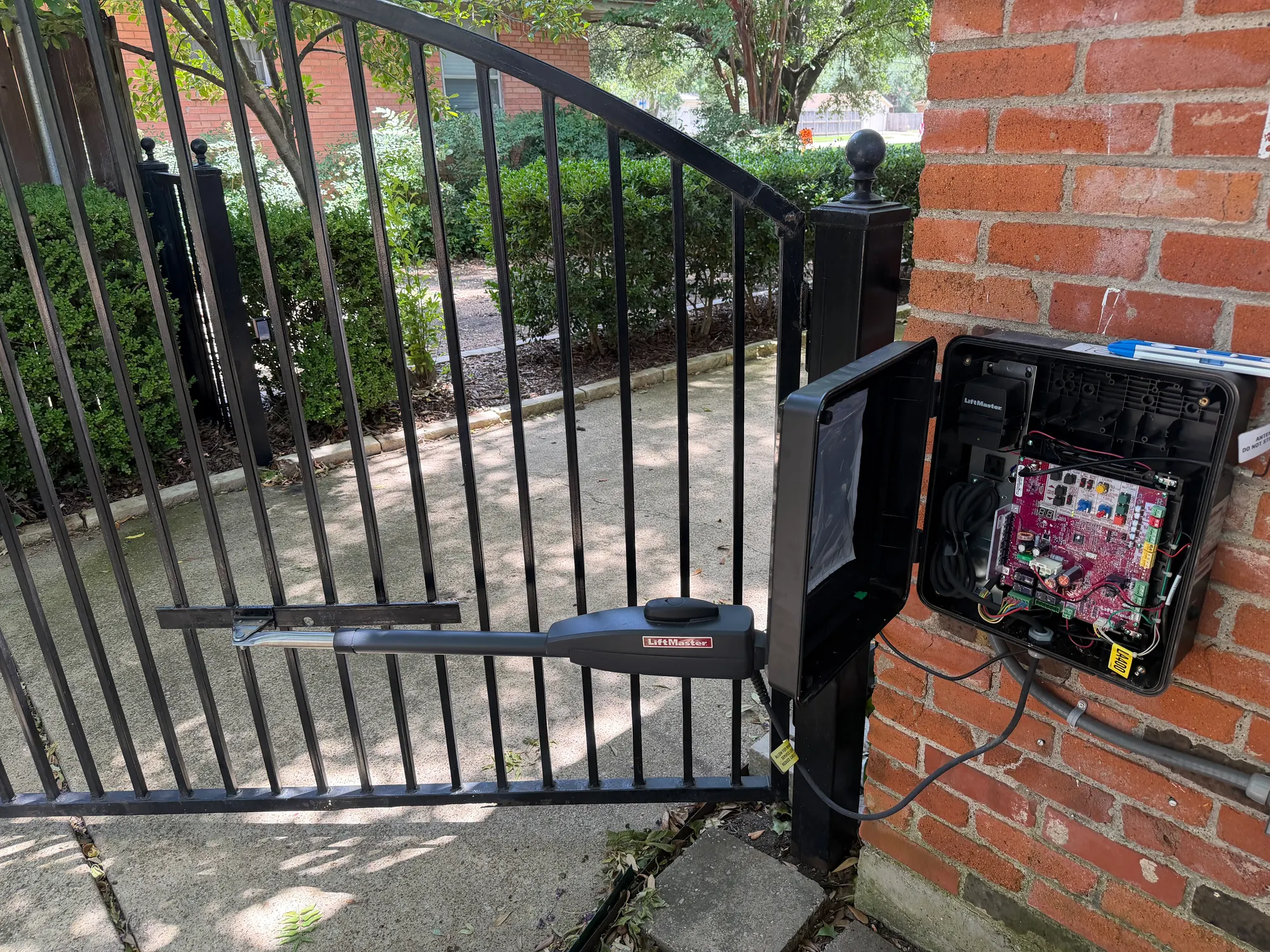 Close view of the open LiftMaster control box showing the control board and its two-digit diagnostic display, with the yellow LA400 model label on the housing and the operator arm attached to the iron gate behind