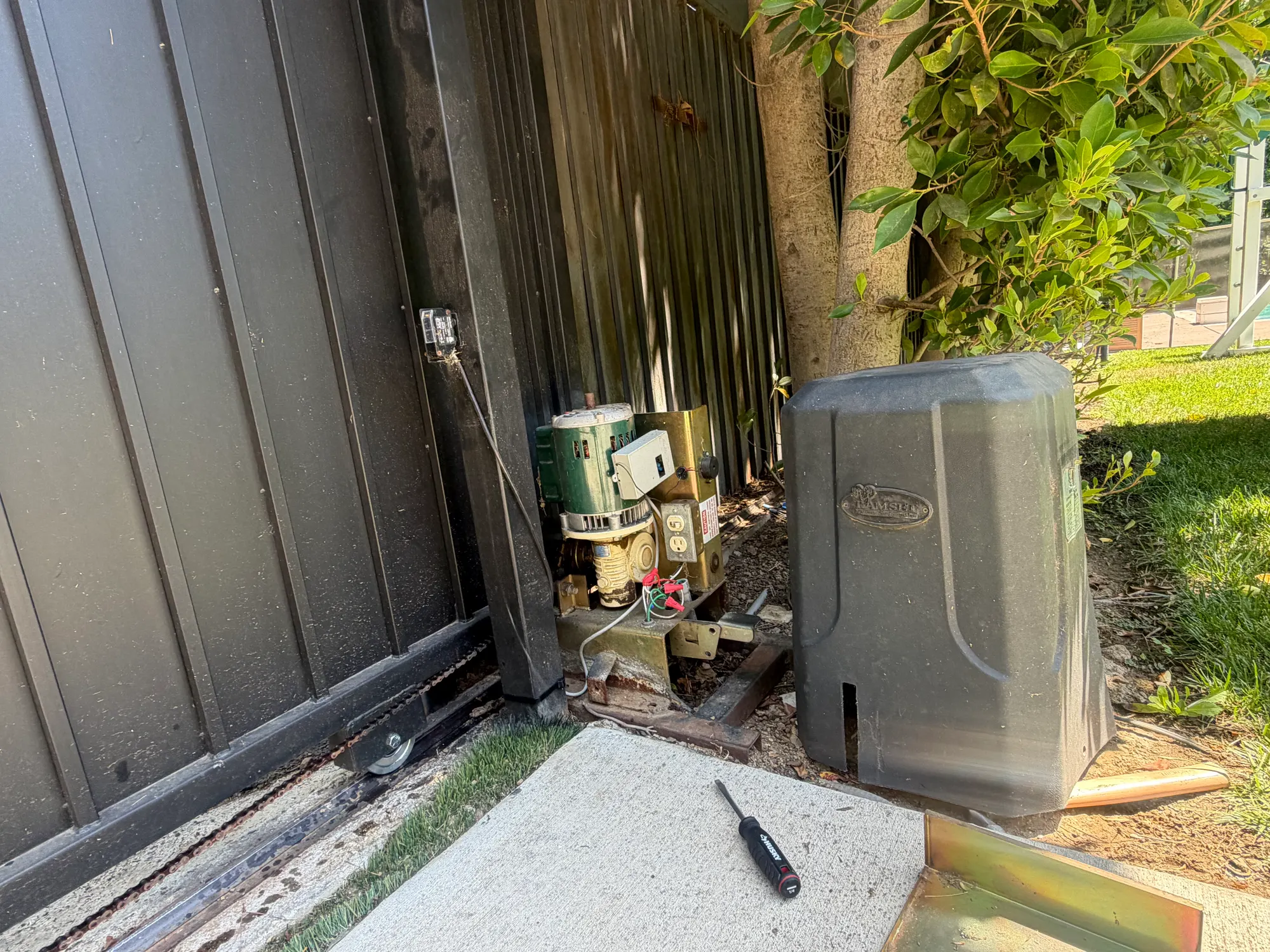 The base of the slide gate lifted away from the track, showing the roller mounting and the operator housing behind
