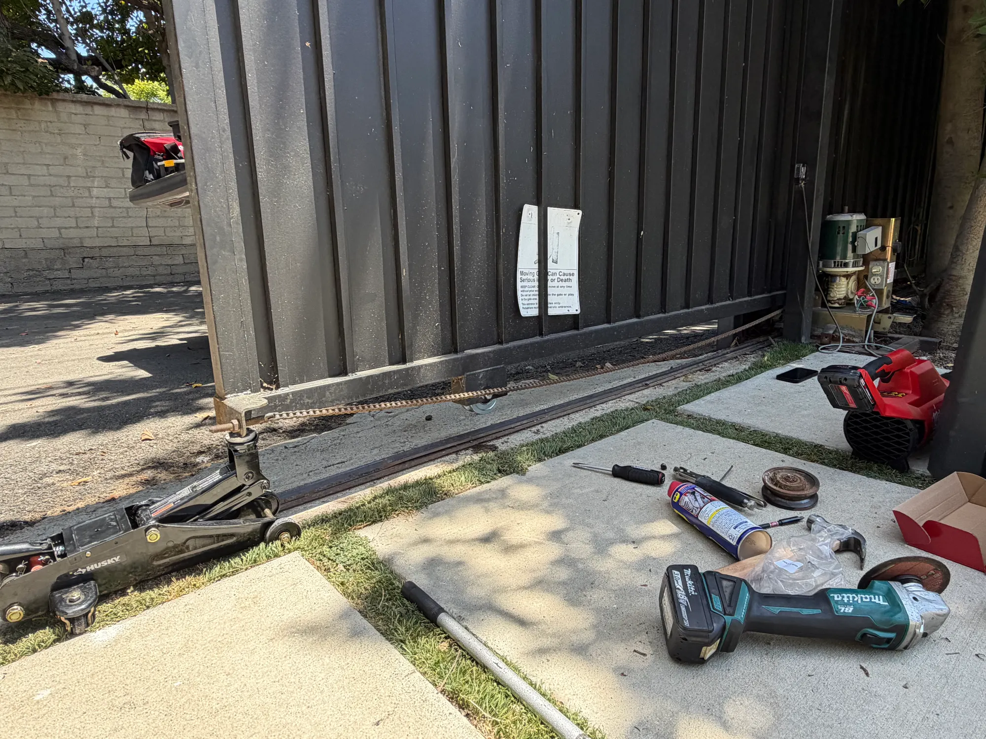 The gate track and roller assembly at ground level with hand tools and a cordless driver laid out during the repair