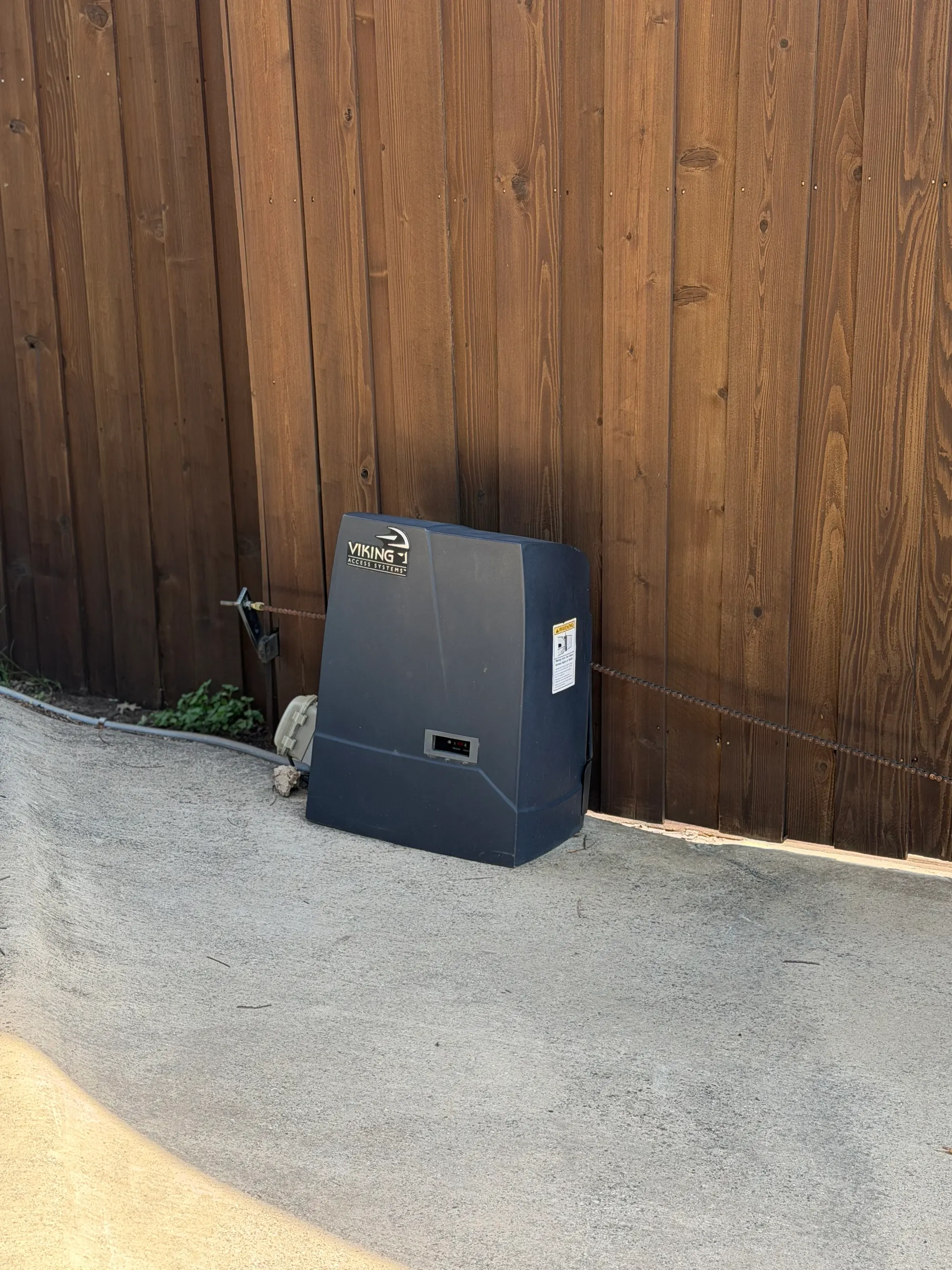 A solar charging panel mounted near a gate operator on a rural driveway