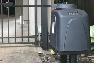 A Viking slide gate operator in a dark grey housing with the Viking name on the front, installed on a concrete pad against a timber fence
